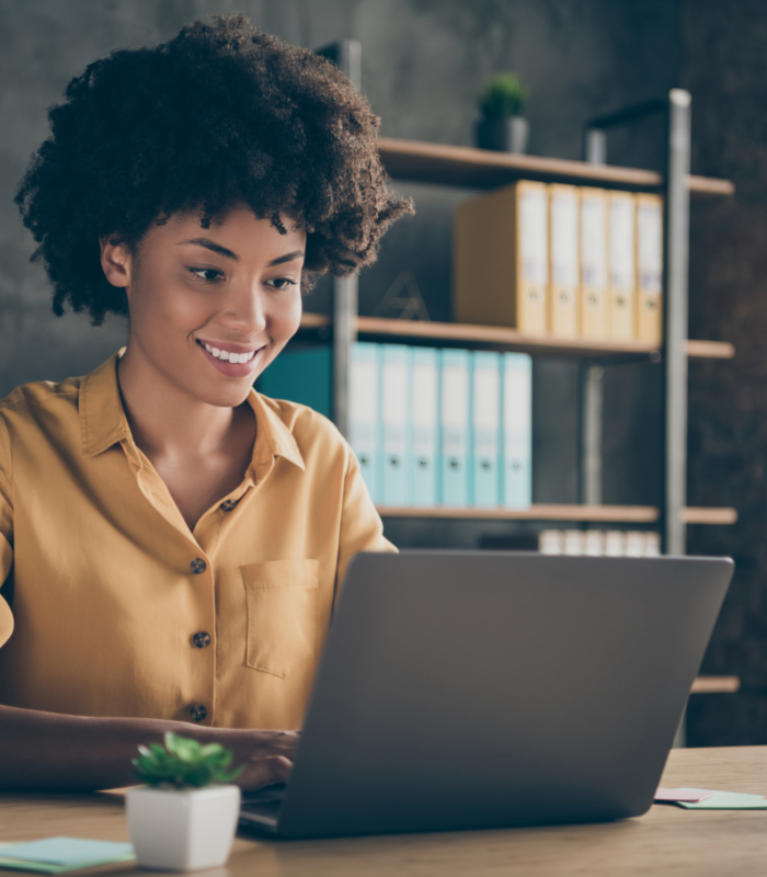 Photo of cheerful positive, mixed-race girl smiling toothily working on presentation about her corporation using laptop on desktop